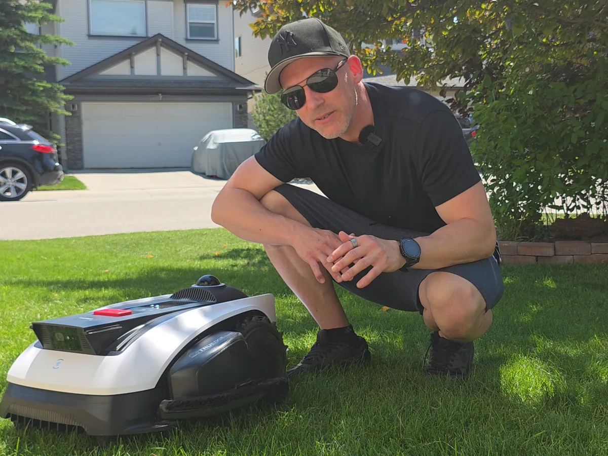 Brad kneeling beside the ECOVACS GOAT O1000 robot mower in his yard